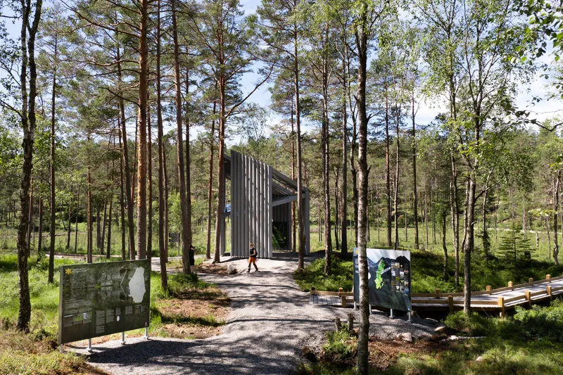 Gravel path leading to a vertical timber slatted chapel set among tall pine trees