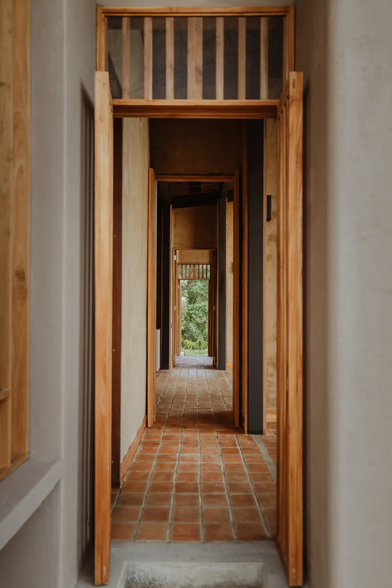 Corridor framed by timber doorways with terracotta tile flooring leading to distant greenery