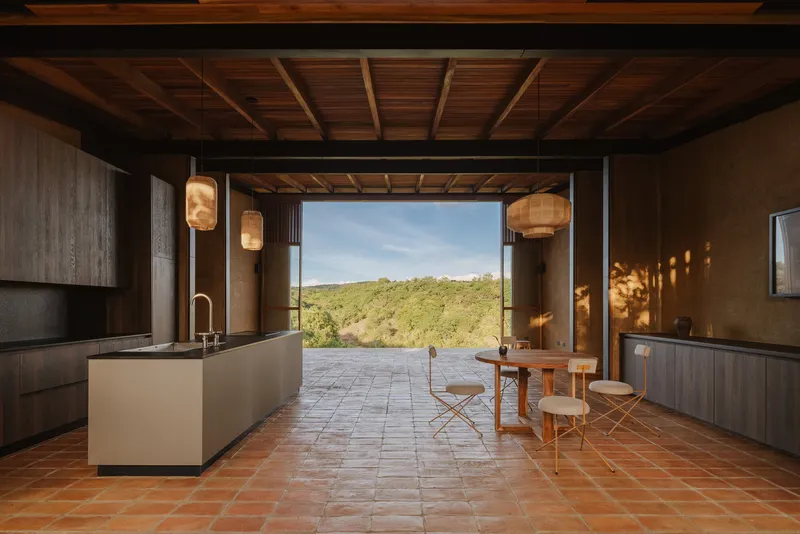 Open-plan living space with terracotta tile floor and timber ceiling framing view to landscape beyond