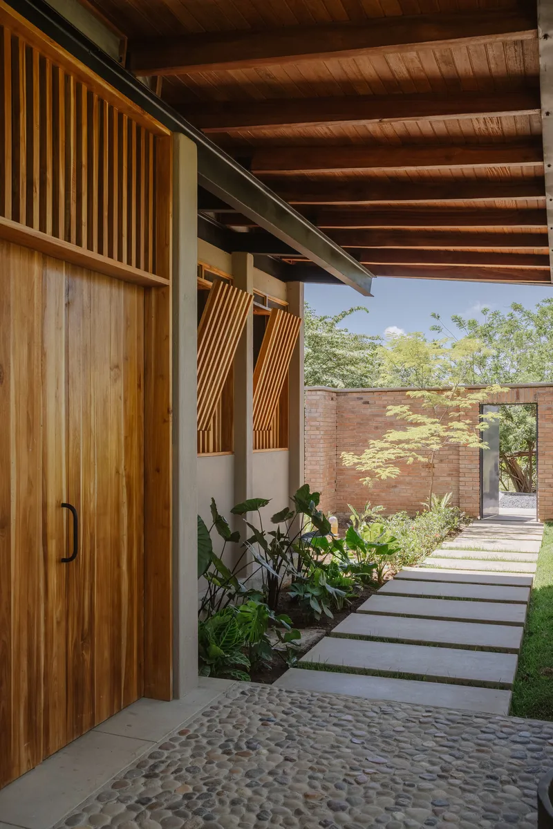 Timber facade with slatted screens and planted bed along stepping stone path leading to brick wall