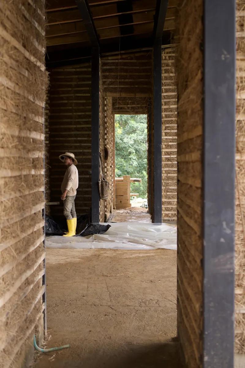Worker in yellow boots standing in rammed earth corridor with exposed timber ceiling during construction