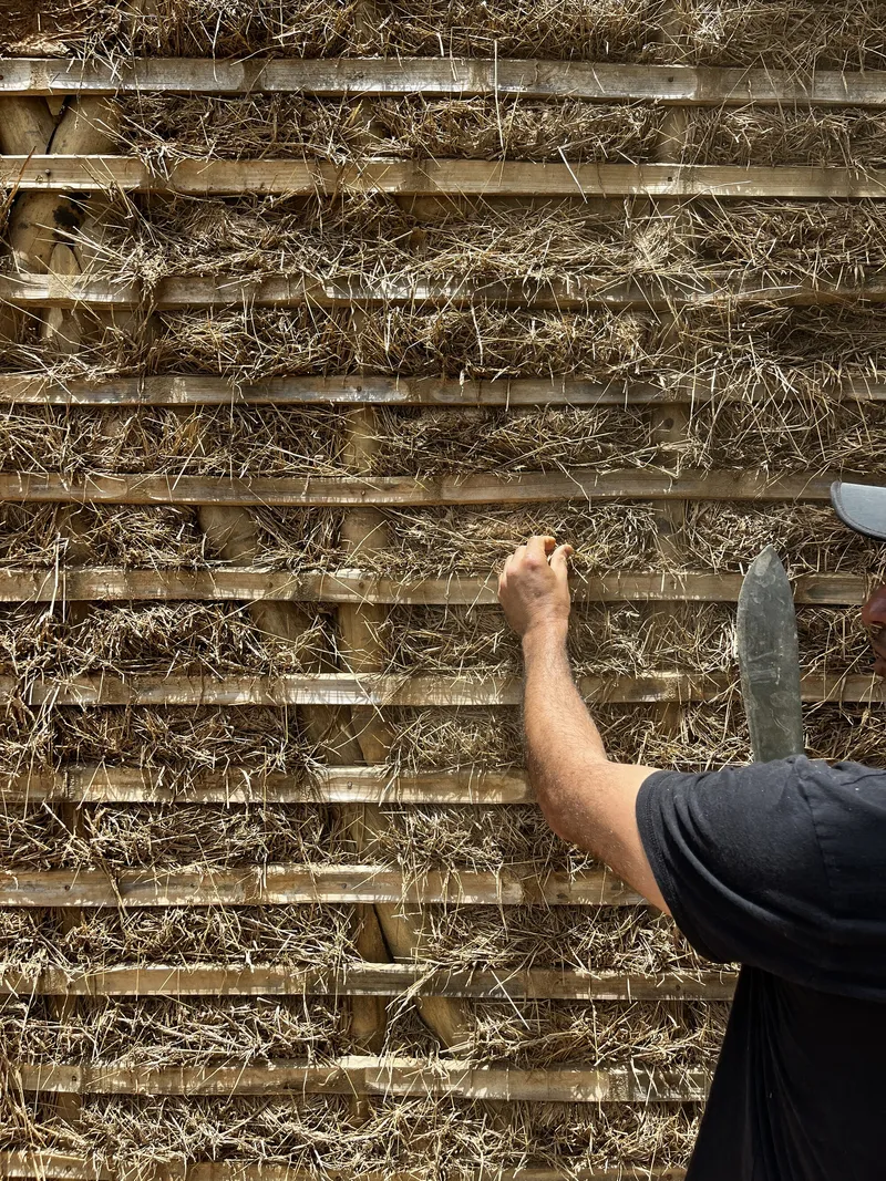 Hand pressing straw and clay mixture into horizontal bamboo framework infill from below