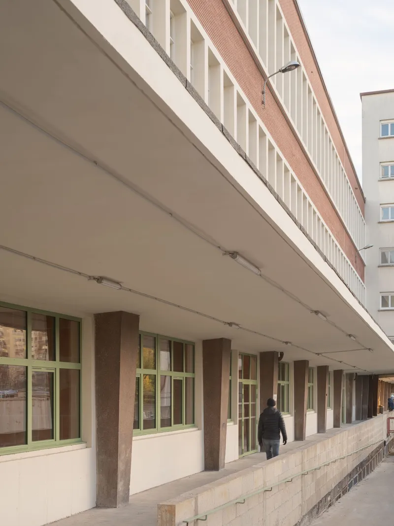 Covered walkway with concrete columns, green window frames and white soffit under cloudy sky