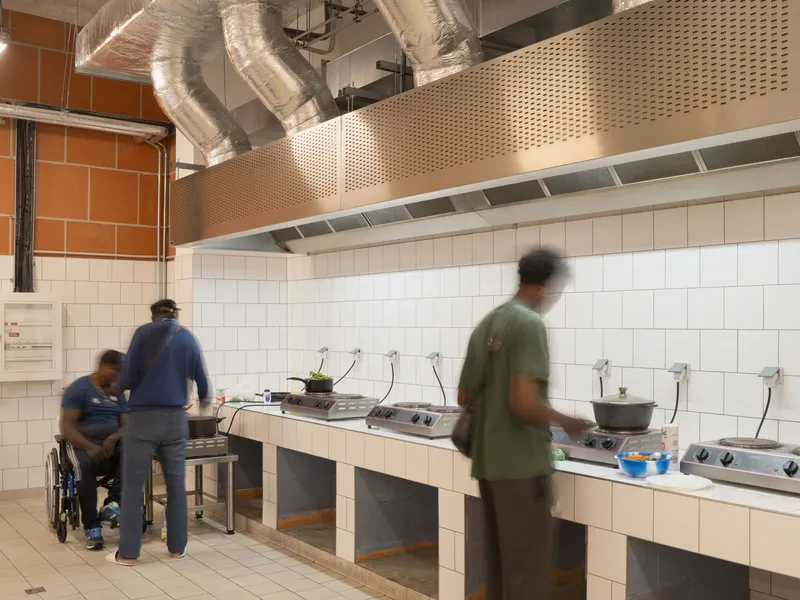 Accessible kitchen with white subway tile walls, perforated metal hood and people cooking