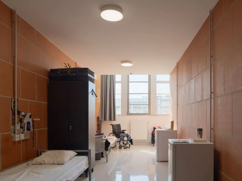 Residential room with terracotta tile walls, metal bed, black wardrobe, and wheelchair visible by window