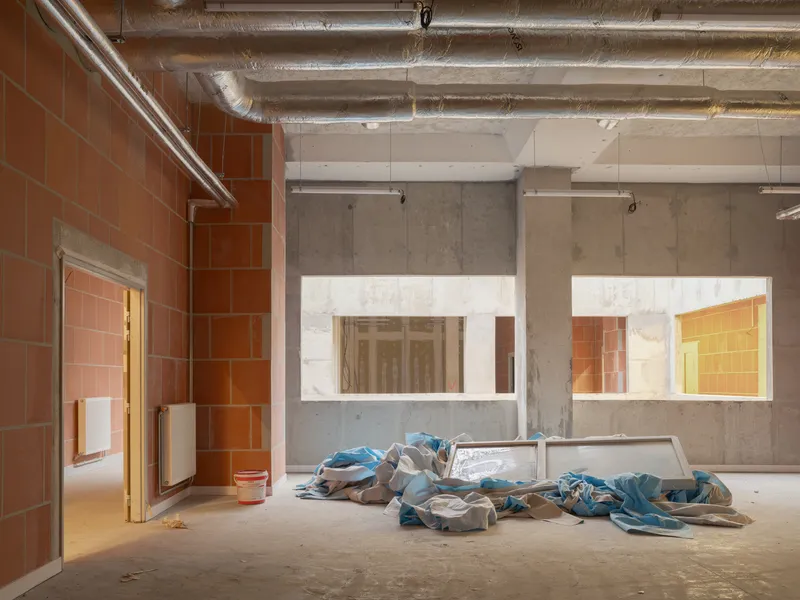 Unfinished interior space with terracotta tile walls, concrete partitions, exposed ductwork, and construction debris on floor