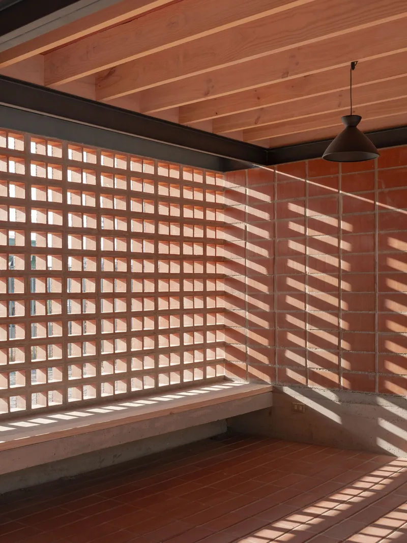 Corner seating nook with terracotta block wall and timber bench under striped afternoon light