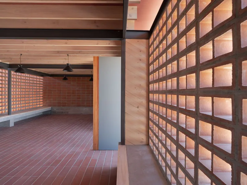 Glowing terracotta block wall alongside timber ceiling and concrete floor with pendant lights