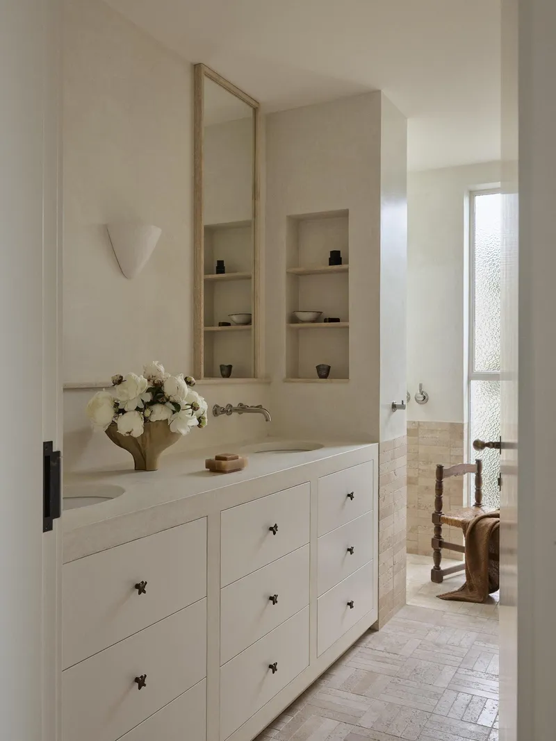 Bathroom vanity with white drawers and recessed wall niches beneath a tall mirror and sconce