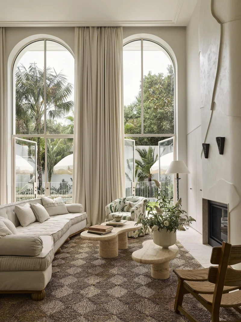 Double-height living room with tall arched windows and curved white fireplace flanked by black sconces