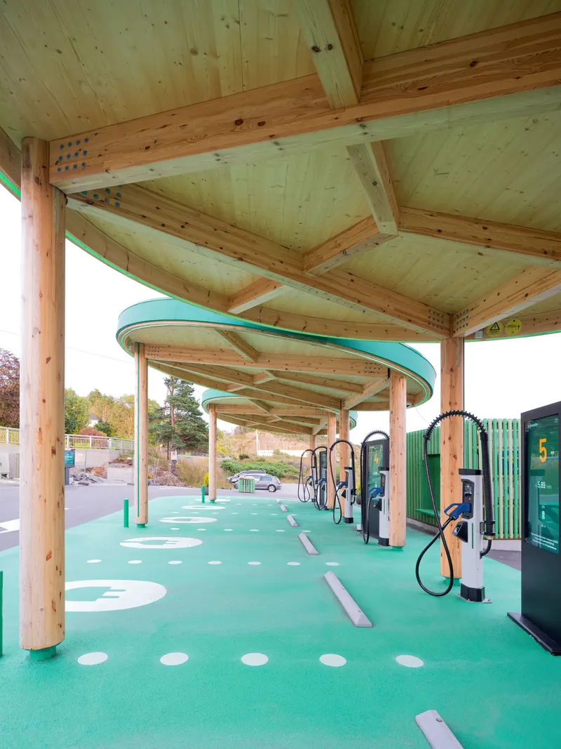 Underside view of the timber canopy structure showing exposed joinery and radiating beams over the charging stations