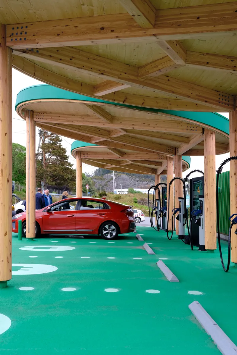 Interior view beneath the timber canopy with a red electric vehicle parked at a charging post