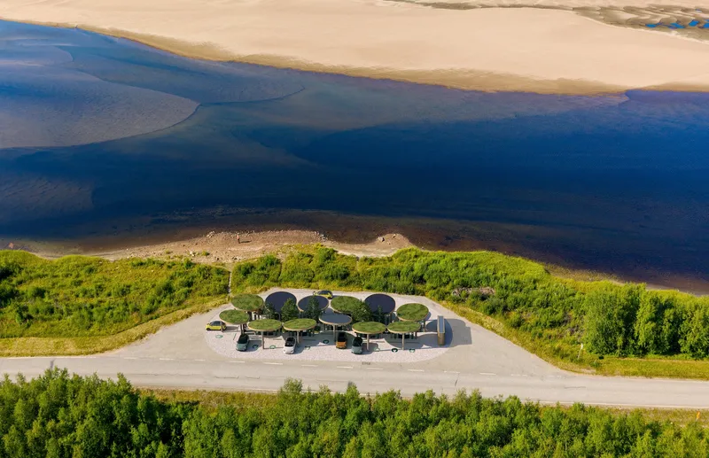 Aerial view of the charging station with circular canopies situated between a coastal road and the blue waterfront