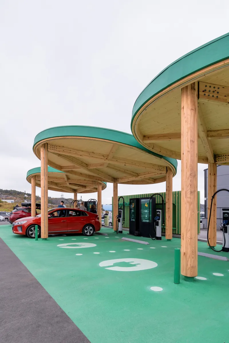 Angled view of the three circular canopies with timber columns and a red vehicle charging beneath the overhangs