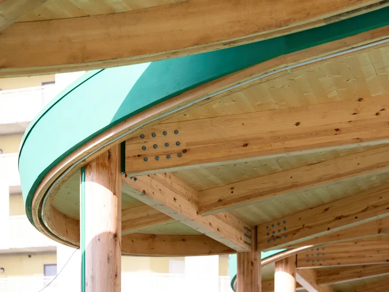 Close-up of the curved timber beams and teal metal edge meeting at the column connection