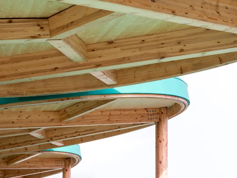 Underside of two circular timber canopies with exposed radial beams and teal fascia bands
