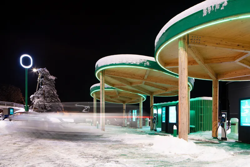 Night view of the illuminated charging station canopies with snow on the ground and a frost-covered tree