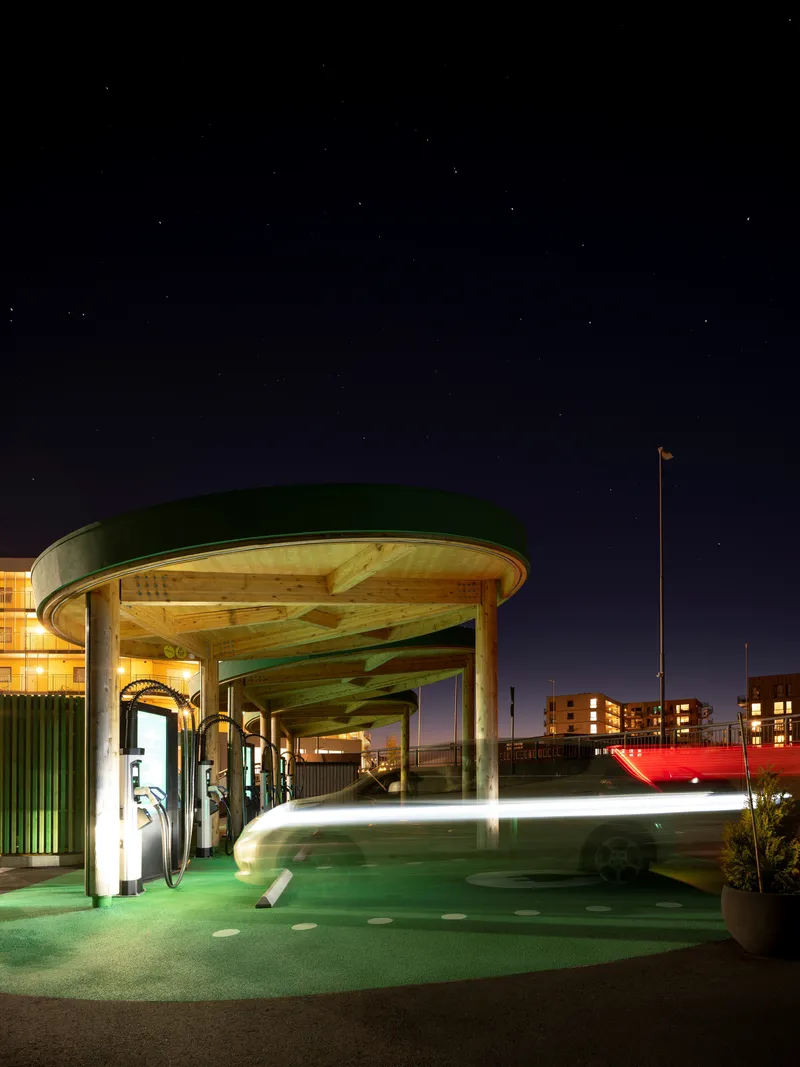Circular timber canopy over electric charging stations illuminated under a starry night sky
