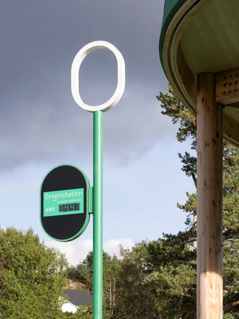 Green steel signage pole with circular ring light beside timber column and canopy edge