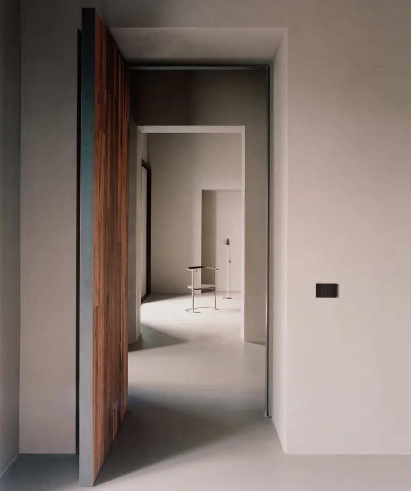 Open timber door revealing a sequence of pale plastered rooms with polished floor