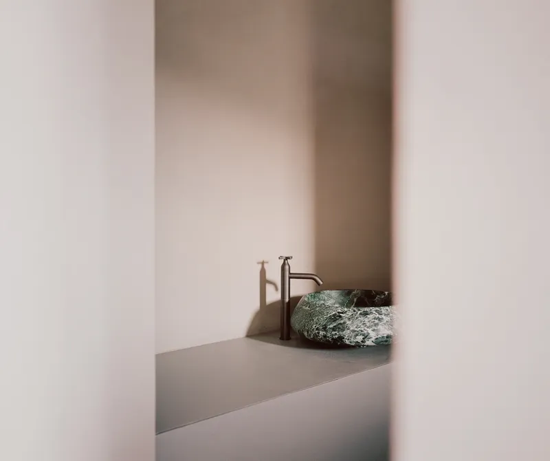 Stone vessel sink with brass faucet on a grey counter framed by pale plastered walls