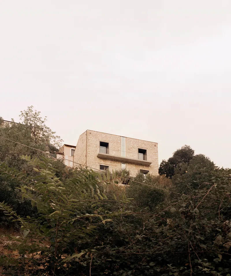 Two-story brick facade with recessed openings above a sloped terrain with trees