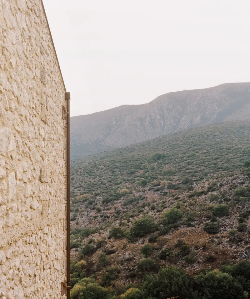 Textured stone wall edge against a mountain slope covered in scrub vegetation