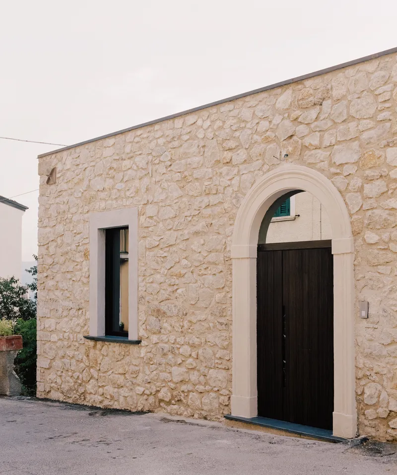 Stone facade with arched doorway and dark metal door beneath an overcast sky