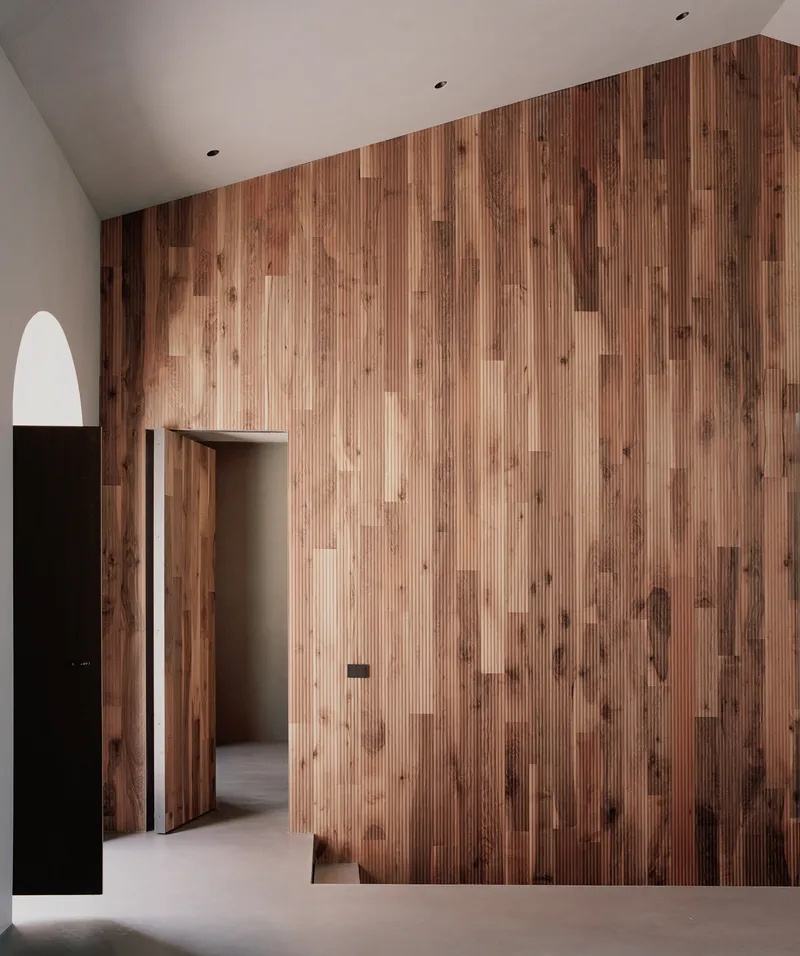 Vertical-grain timber wall with integrated doorway and arched passage framing a view through