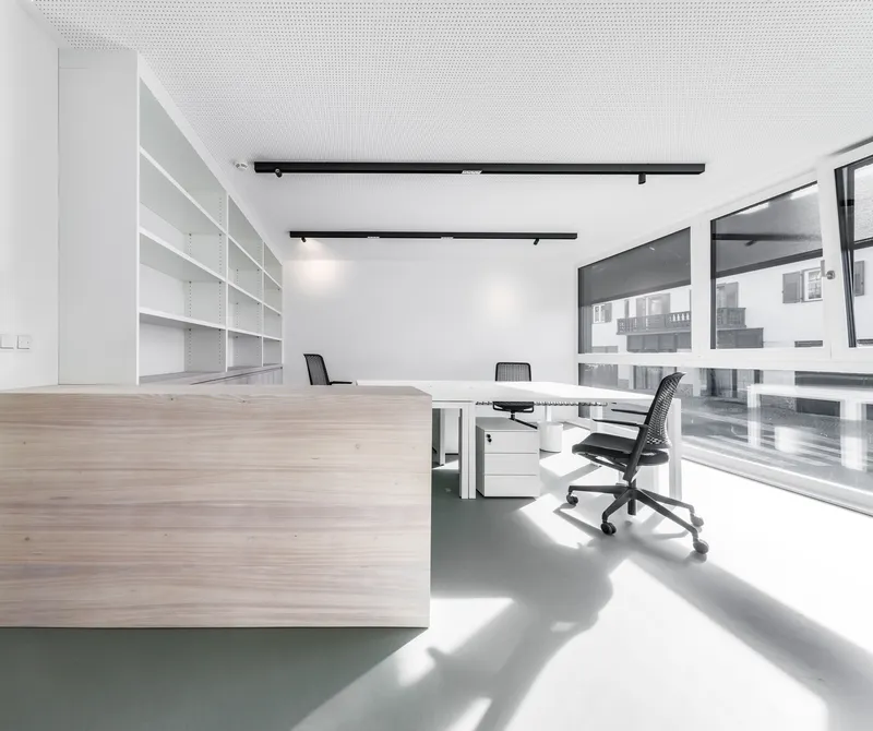 Open office space with white shelving units and grey resin floor beneath black track lighting