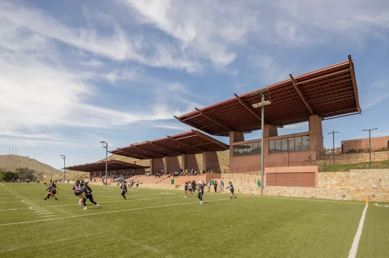 Cantilevered grandstand with exposed timber roof beams supported by concrete columns during a game