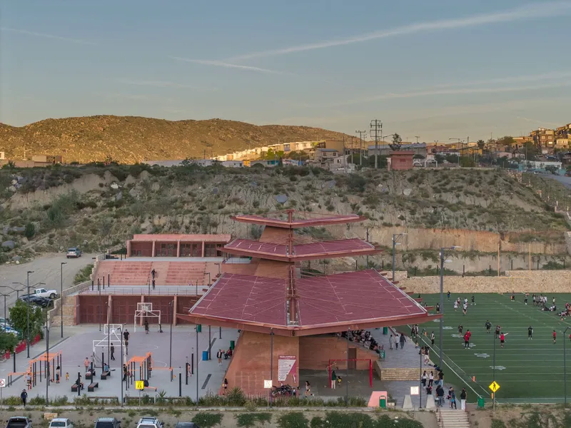 Entry plaza with terraced roofs and stepped retaining walls set against a hillside neighborhood