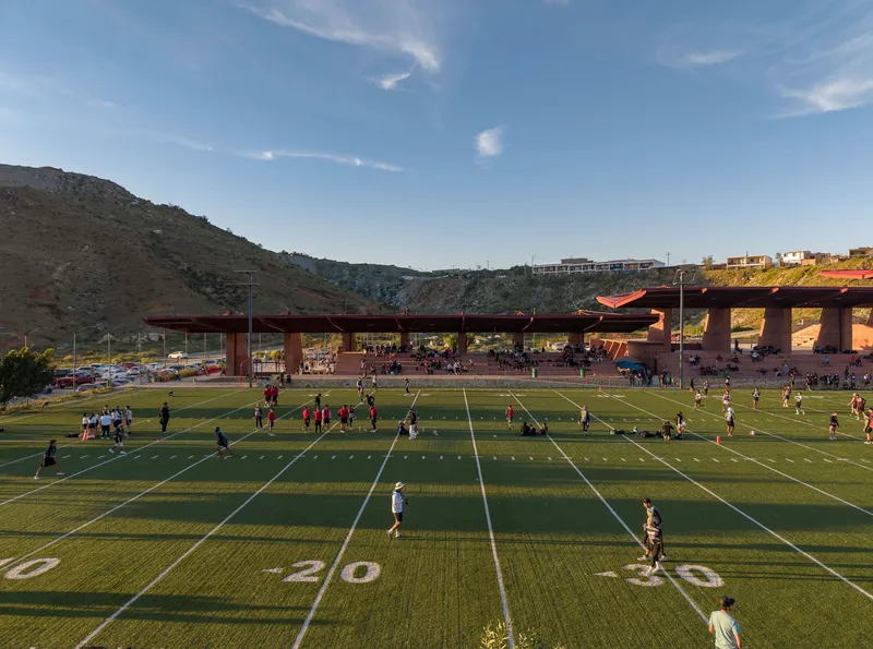 Football field with players practicing beneath the canopy and terraced seating in afternoon light
