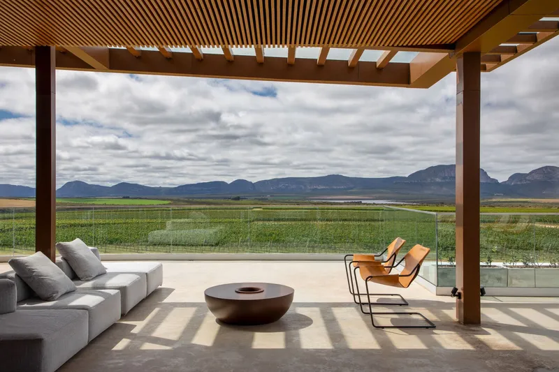 Covered terrace with timber pergola beams overlooking fields and distant mountain range under cloudy sky