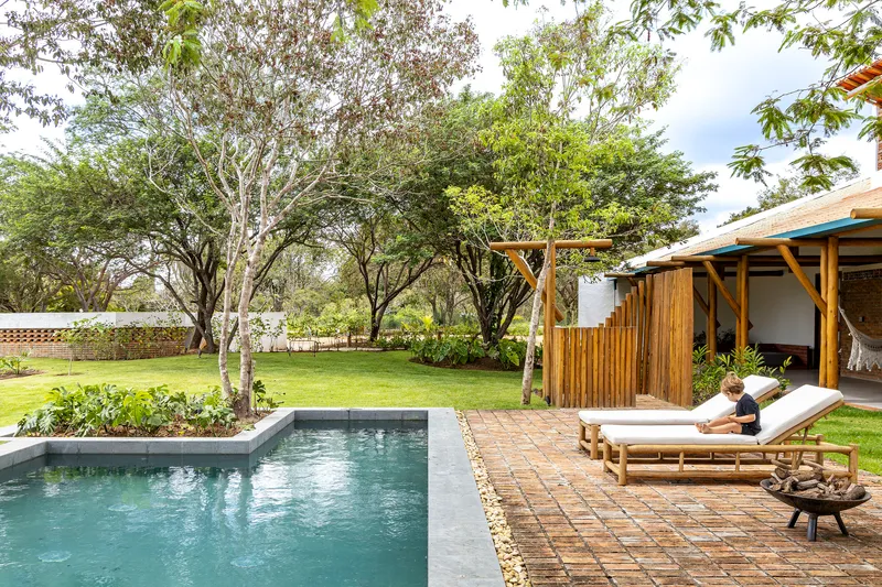 Poolside terrace with brick pavers and bamboo screen wall adjacent to lawn and established trees