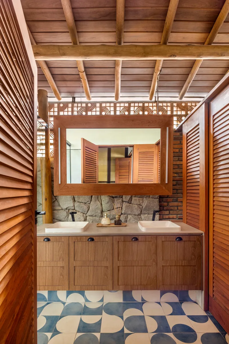Bathroom vanity with double sinks, louvered mirror, and patterned floor tile beneath timber ceiling joists