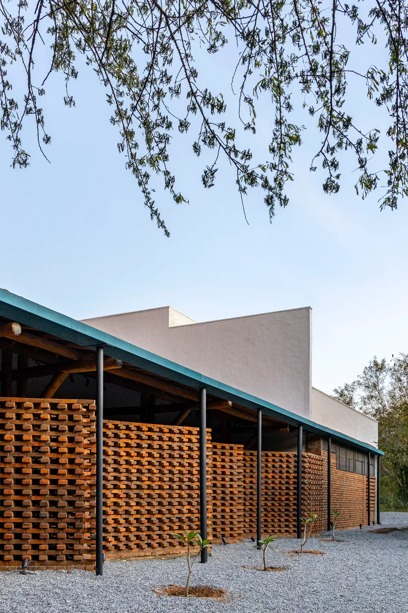 Facade with openwork brick screens under a sloped roof with hanging tree branches framing the view