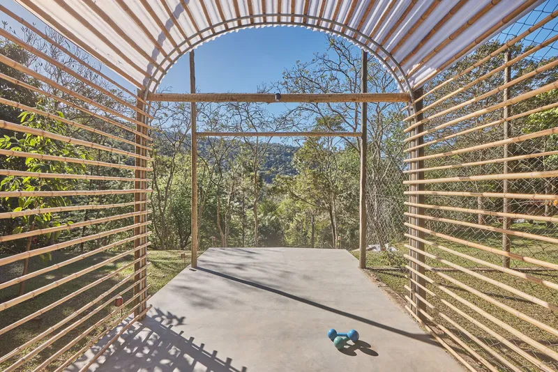 View through the barrel-vaulted timber pavilion with horizontal slats framing the wooded landscape beyond