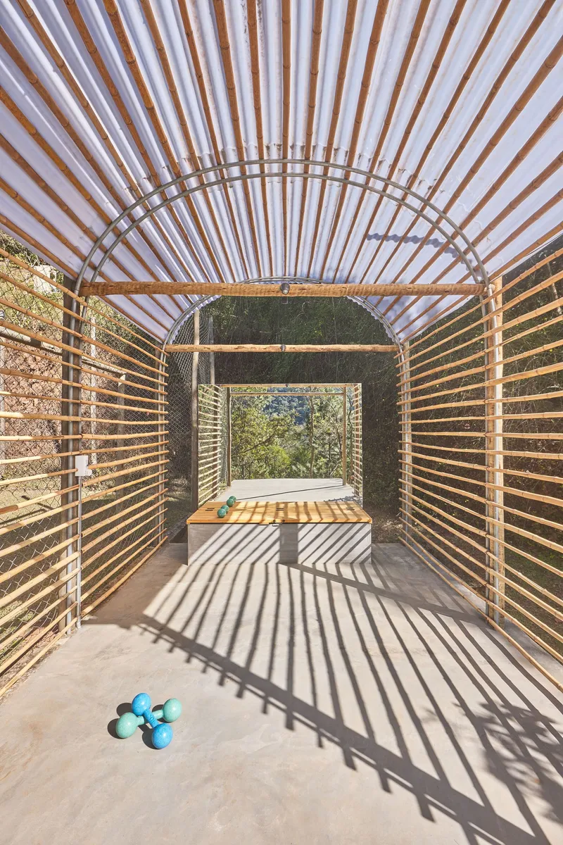 Interior view of the slatted timber pavilion showing layered arched ribs and dappled sunlight on concrete floor