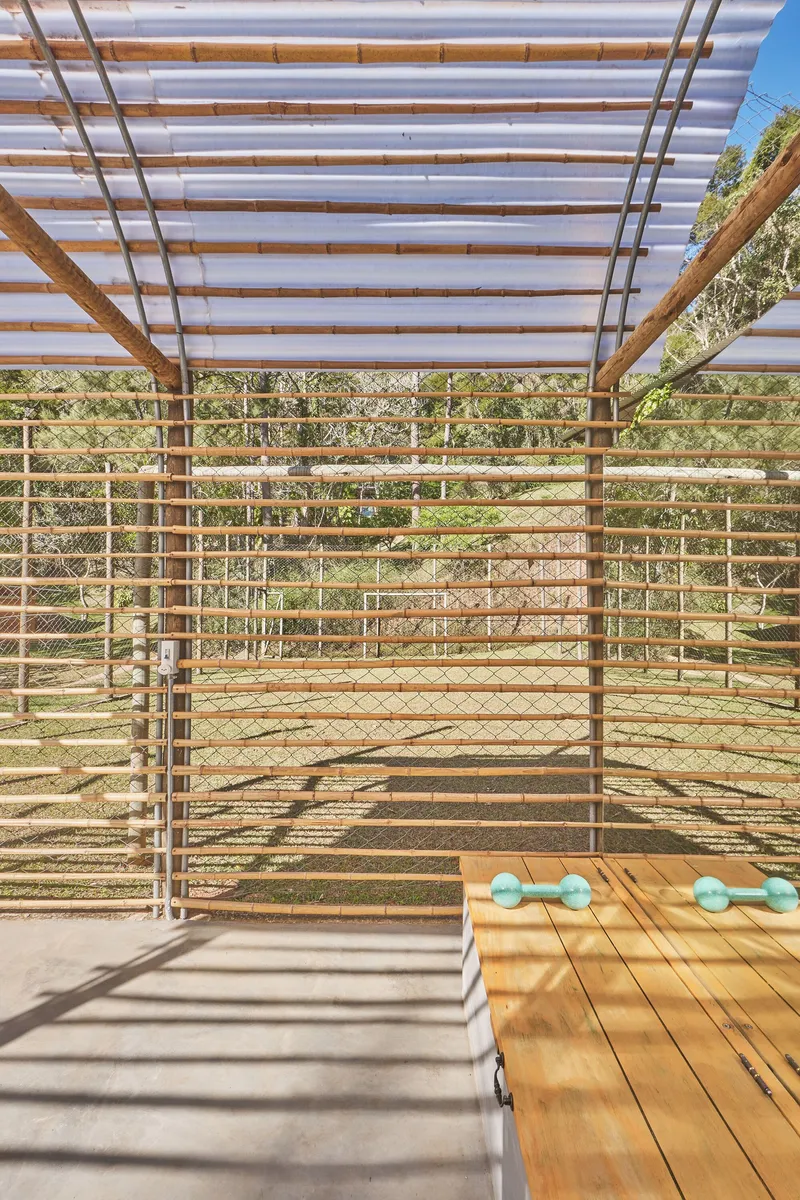 View toward the landscape through horizontal timber slats with corrugated canopy above casting striped shadows
