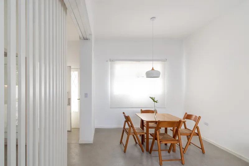 Dining area with wooden table and chairs beside vertical timber slat screen filtering daylight