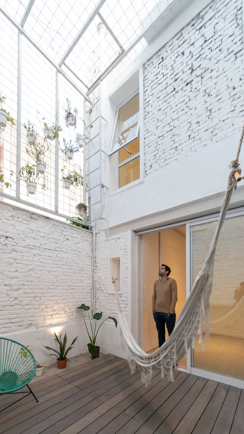 Interior courtyard with timber decking, white painted brick walls, hammock and potted plants under mesh canopy