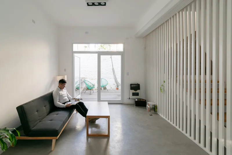 Living room with vertical timber screen and glass doors opening to courtyard with hammock visible beyond