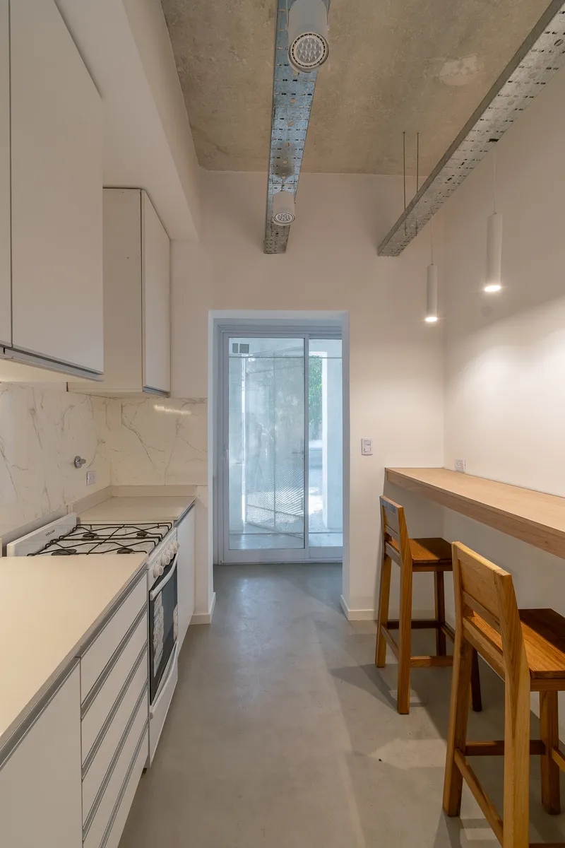 Galley kitchen with exposed concrete ceiling duct running toward a glazed door at the end of the hallway