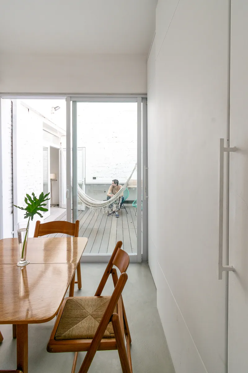 Dining area looking through sliding glass doors to a wooden deck with a hammock and white brick courtyard wall