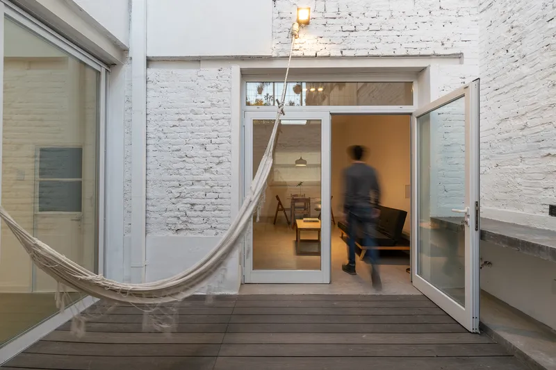 Glazed door opening onto timber deck courtyard with hammock and a blurred walking figure