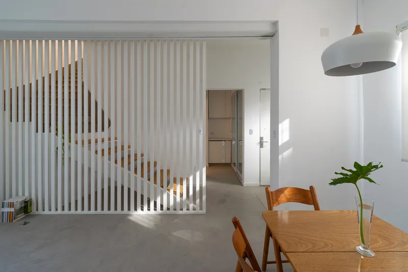 Slatted wood partition revealing staircase and corridor beyond in afternoon sunlight