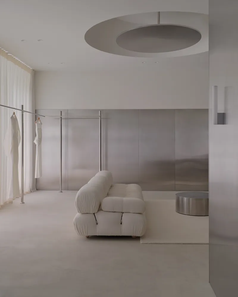 Recessed disc ceiling light above a brushed steel wall panel and freestanding clothing rack