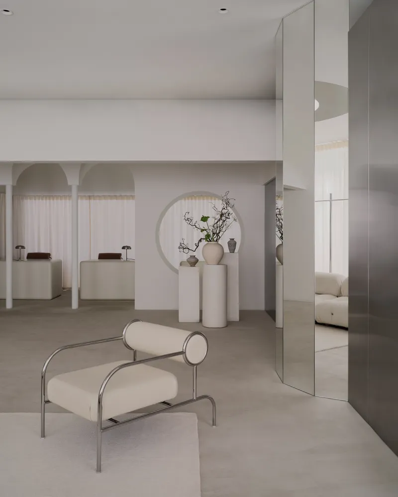 Reception area with tubular steel chair, mirrored panels, and cylindrical pedestals displaying ceramic vessels and branches