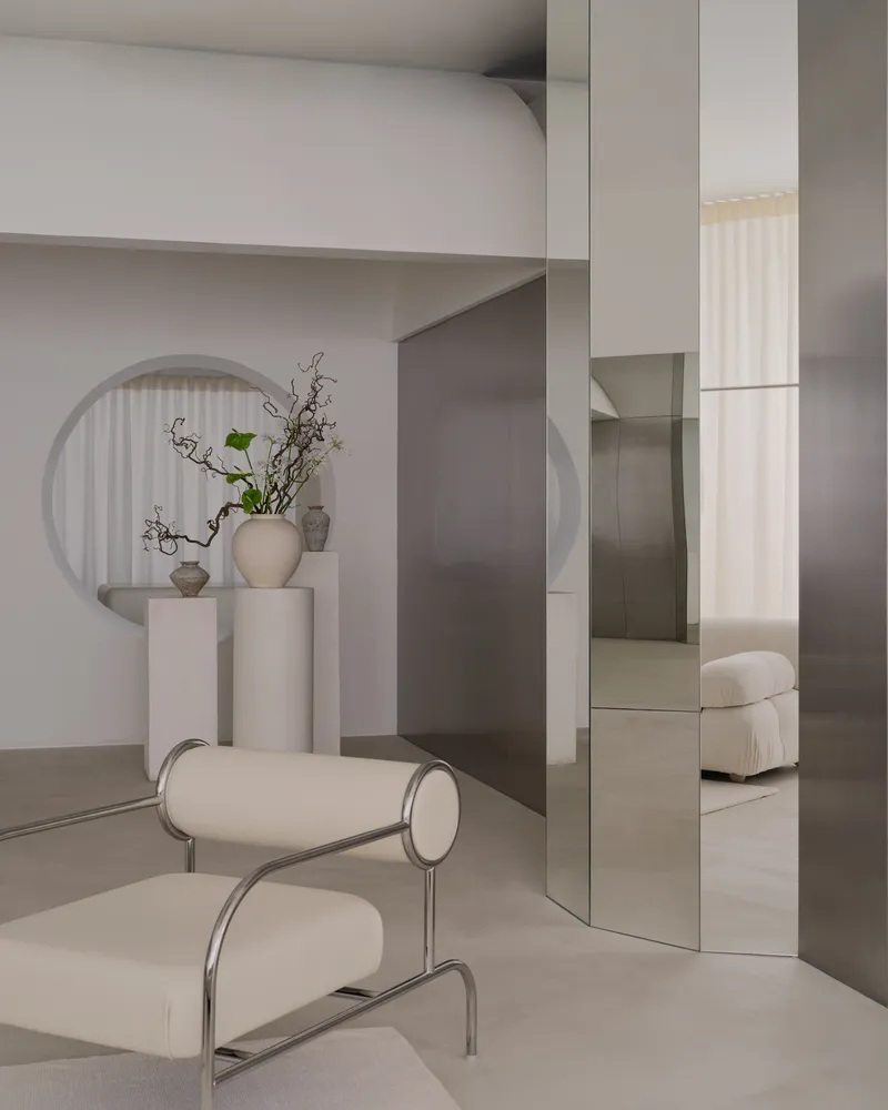 Tubular steel lounge chair in front of mirrored column and circular wall niche with fluted curtain